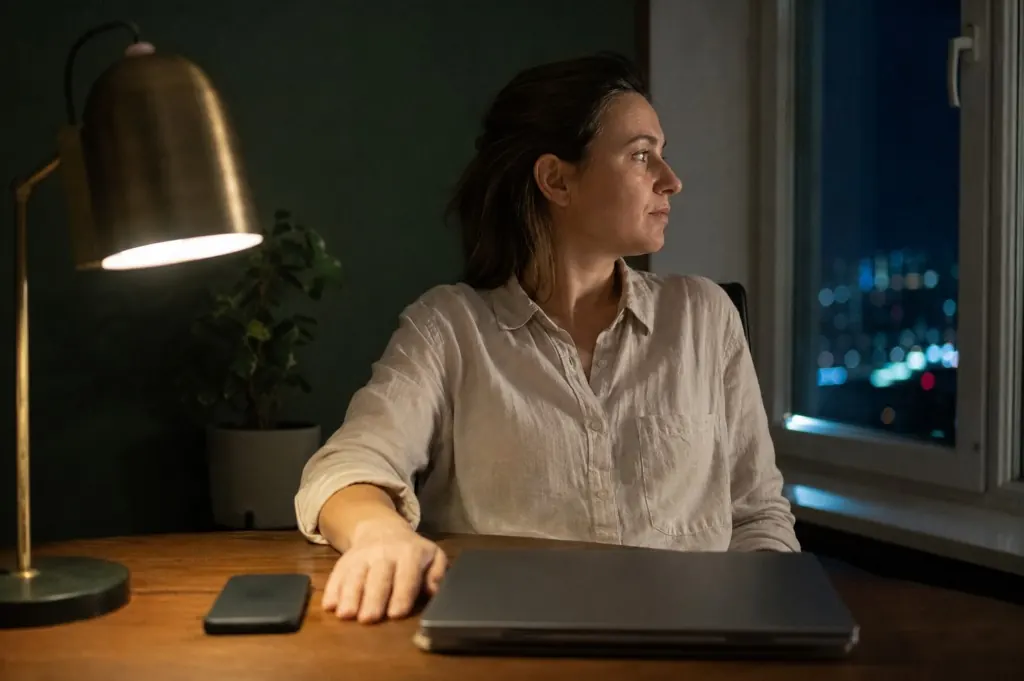 Kobieta przy biurku wieczorem: laptop zamknięty, telefon odłożony, trudność z odłączeniem się od pracy